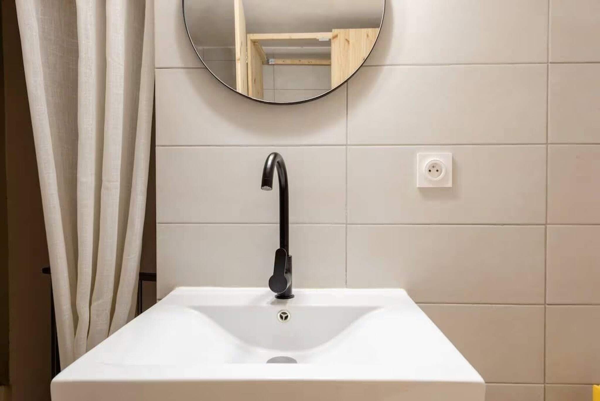 Ein Badezimmer mit einem weißen Waschbecken, einem schwarzen Wasserhahn und einem runden Spiegel an der Wand.
