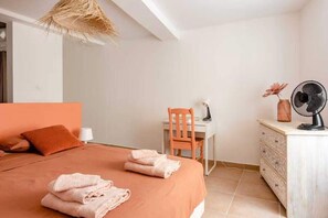 Een slaapkamer met een bed, bureau, stoel, ventilator en een dressoir.