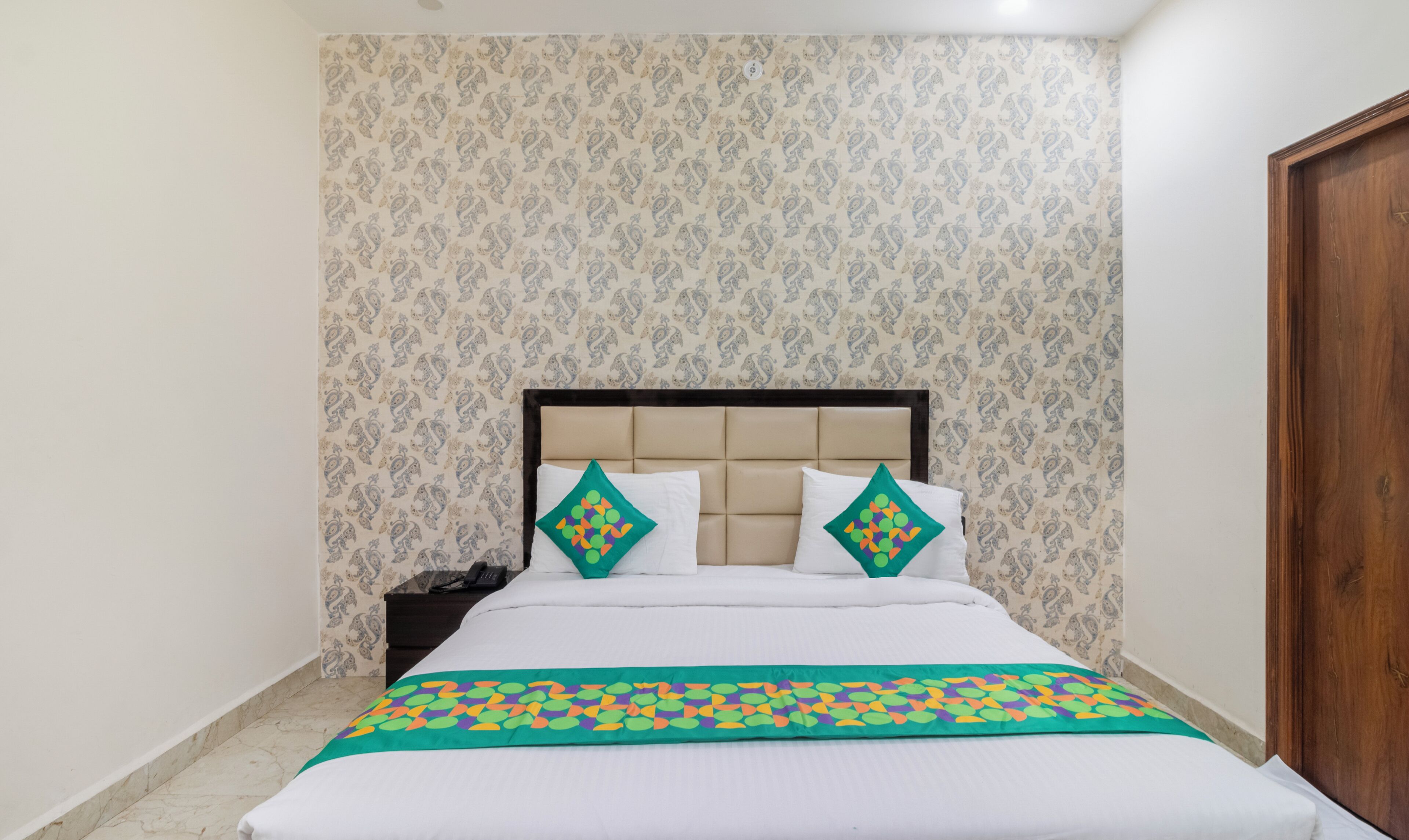 A neatly made bed with a patterned wall and a wooden door.