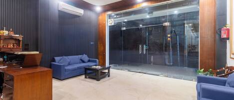 Un hall d’entrée moderne avec un canapé bleu, un bureau en bois et une porte en verre donnant sur l’extérieur.