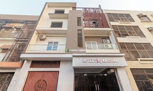 Un hotel con fachada moderna, destacando una entrada principal con puerta grande y un balcón con baranda de vidrio.