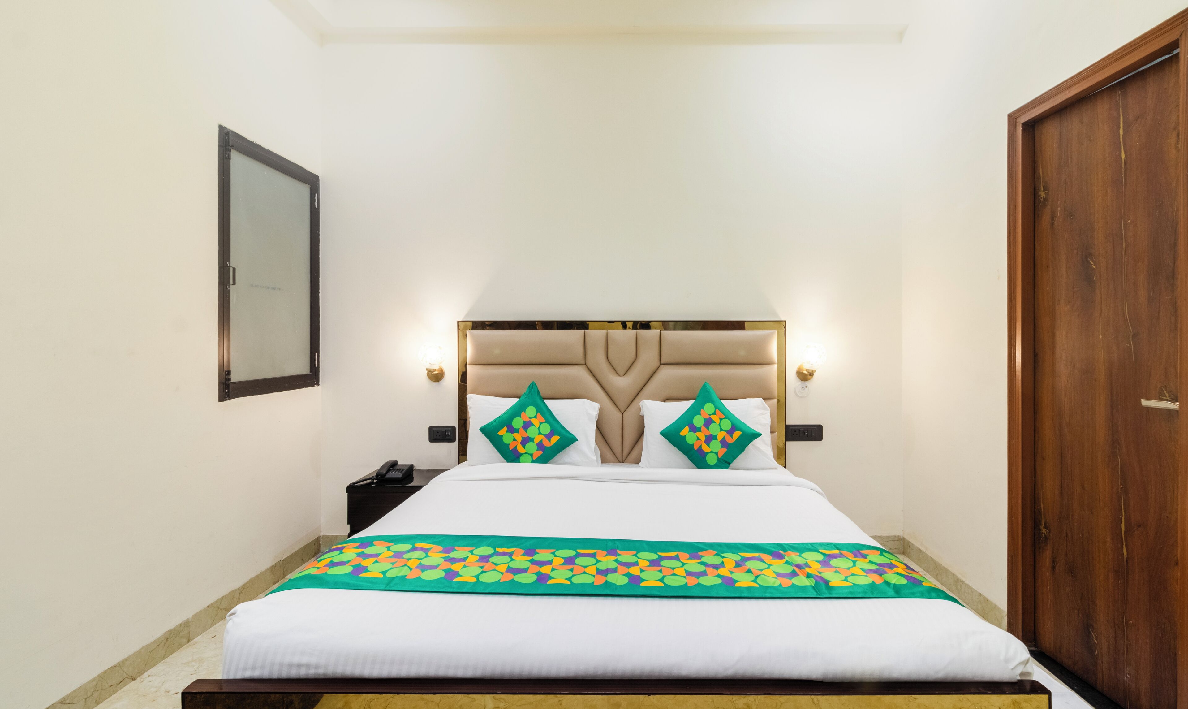 Een hotelkamer met een bed, nachtkastje, lamp en een houten deur.