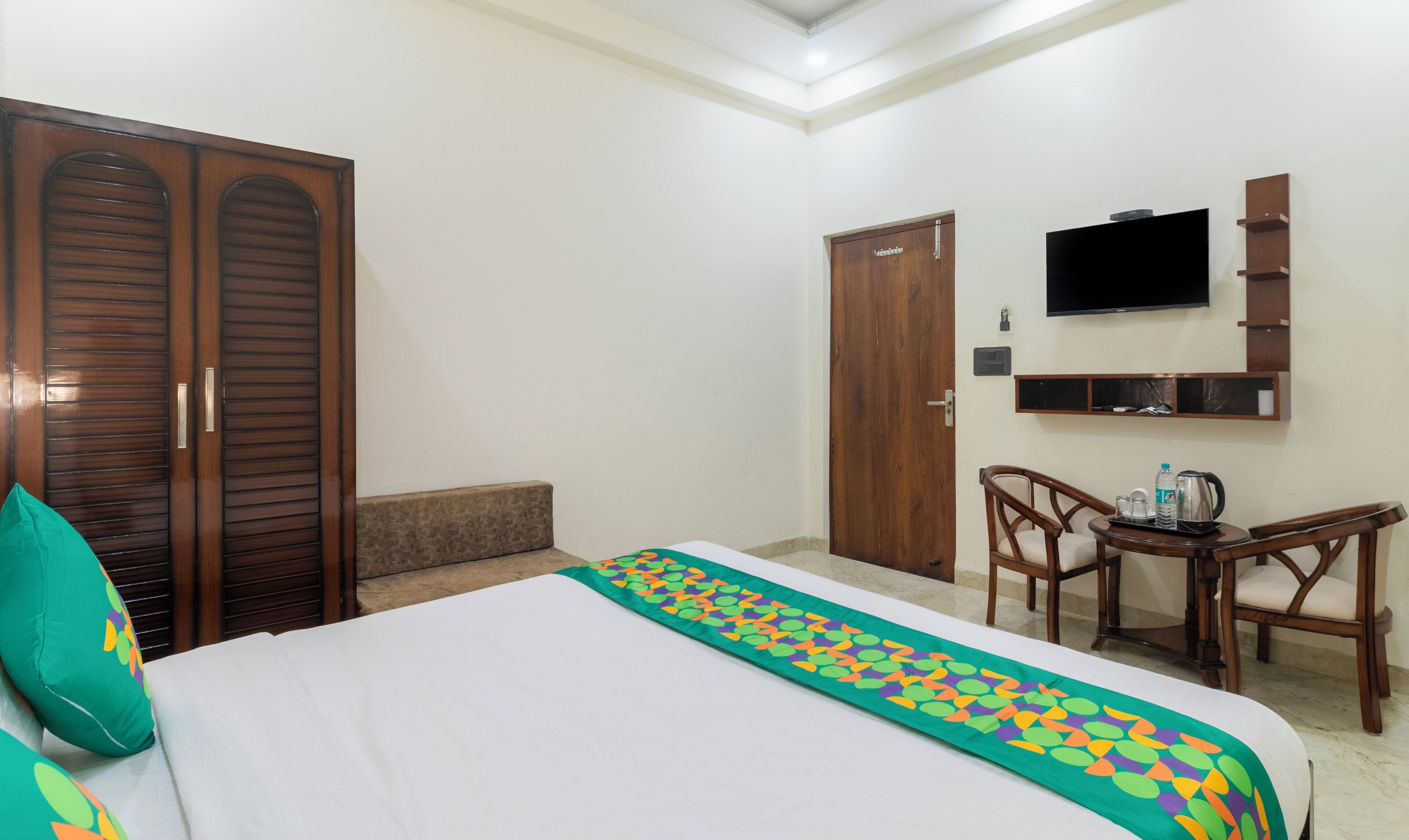 A hotel room with a bed, a desk with a chair, a television, and a wardrobe.