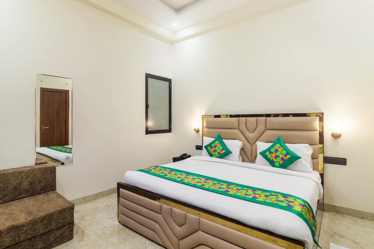 A hotel room with a bed, a mirror, a bedside table, and a brown sofa.