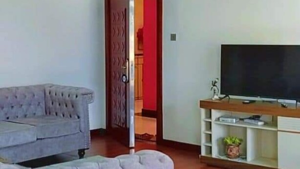 A living room with a grey sofa, a television on a wooden stand, and a red door leading to another room.
