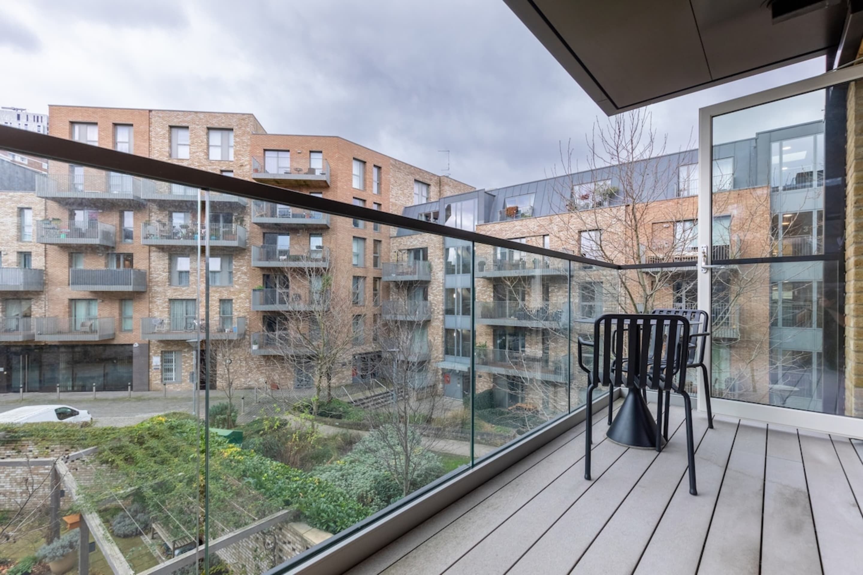 Ein Balkon mit Blick auf moderne Wohngebäude, einer Glasbrüstung und einem schwarzen Stuhl.