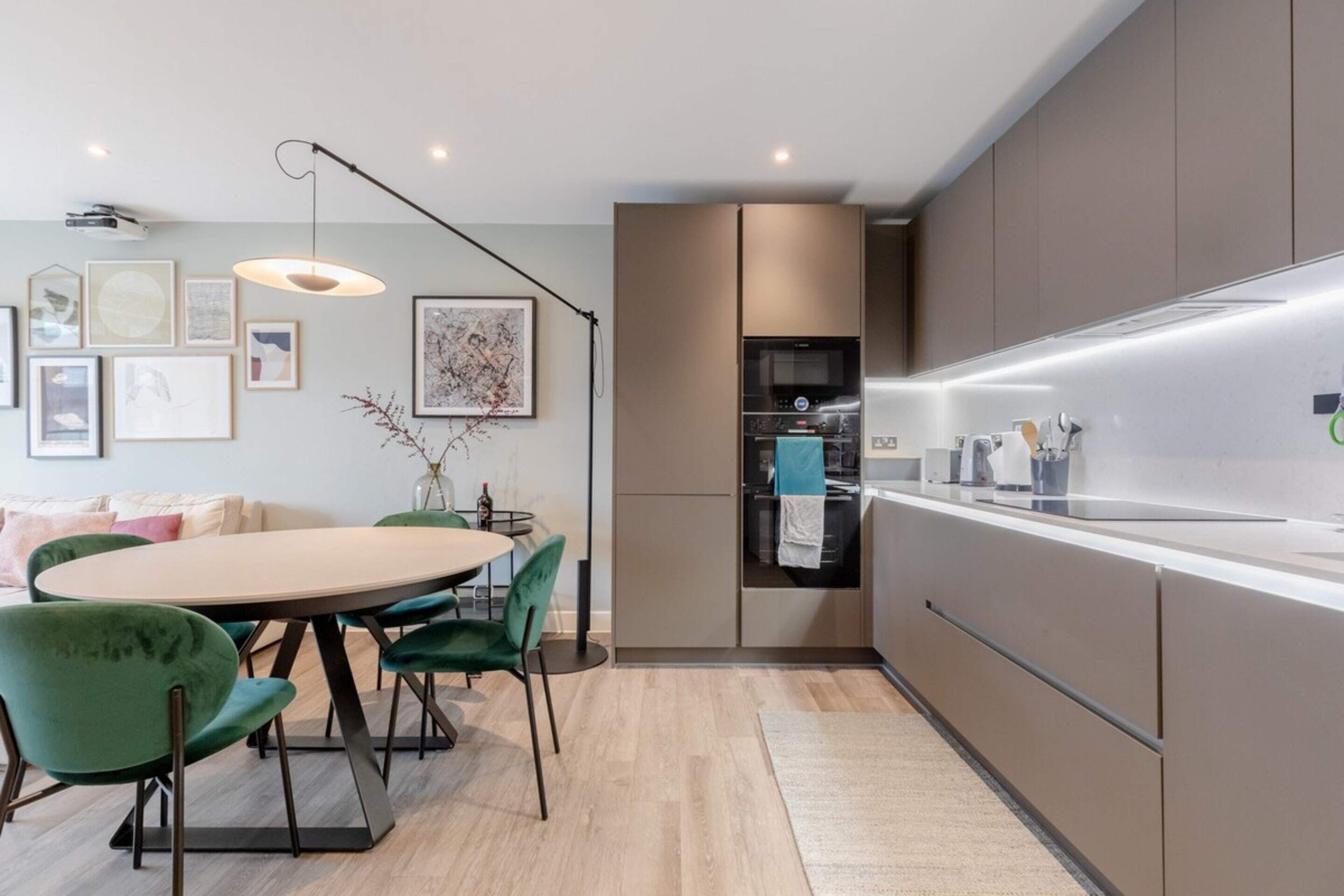 A modern kitchen with a built-in oven and microwave, a dining area with a round table and chairs, and a light fixture above the table.