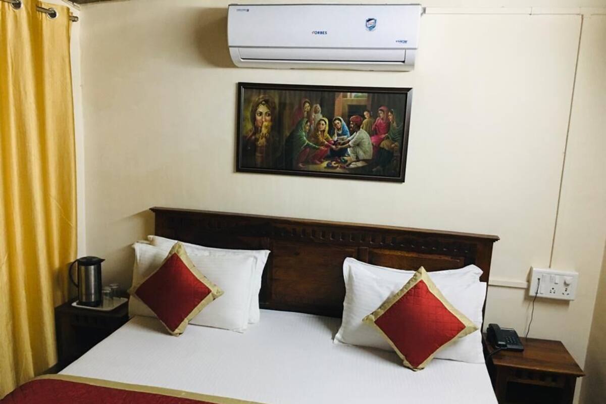 Una habitación de hotel con una cama, un cuadro en la pared, un aire acondicionado y una mesita de noche con un teléfono.