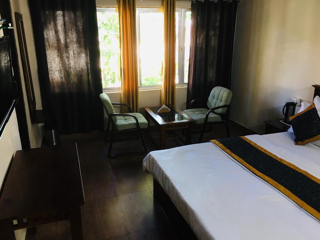 A hotel room with a bed, two chairs, a small table, and a window with curtains.