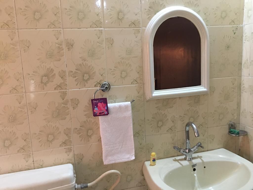 A bathroom with floral patterned tiles, a white sink, and a window above the mirror.