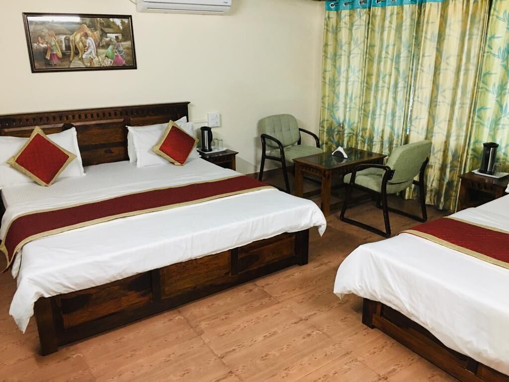 A hotel room with two beds, a wooden floor, a table, chairs, and a curtain.