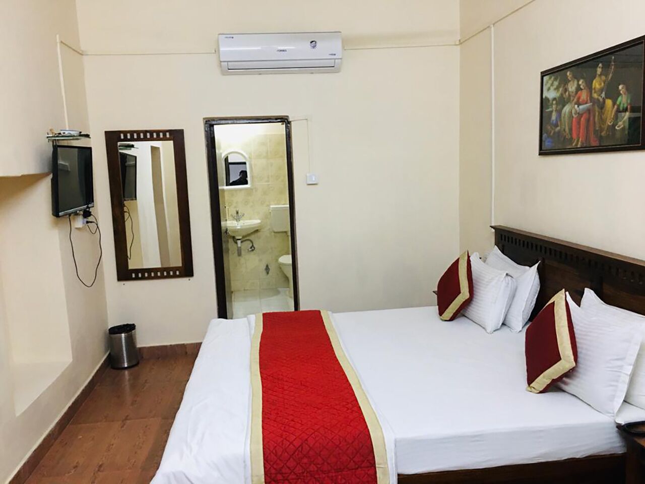 Habitación de hotel con una cama, un espejo, un equipo de aire acondicionado y un cuadro en la pared.