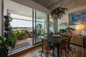 A dining area with a table and chairs, surrounded by potted plants and a large window with a view of buildings. - Brunswick Retreat! 5th Floor 1-bed Unit w Parking (Brunswick)