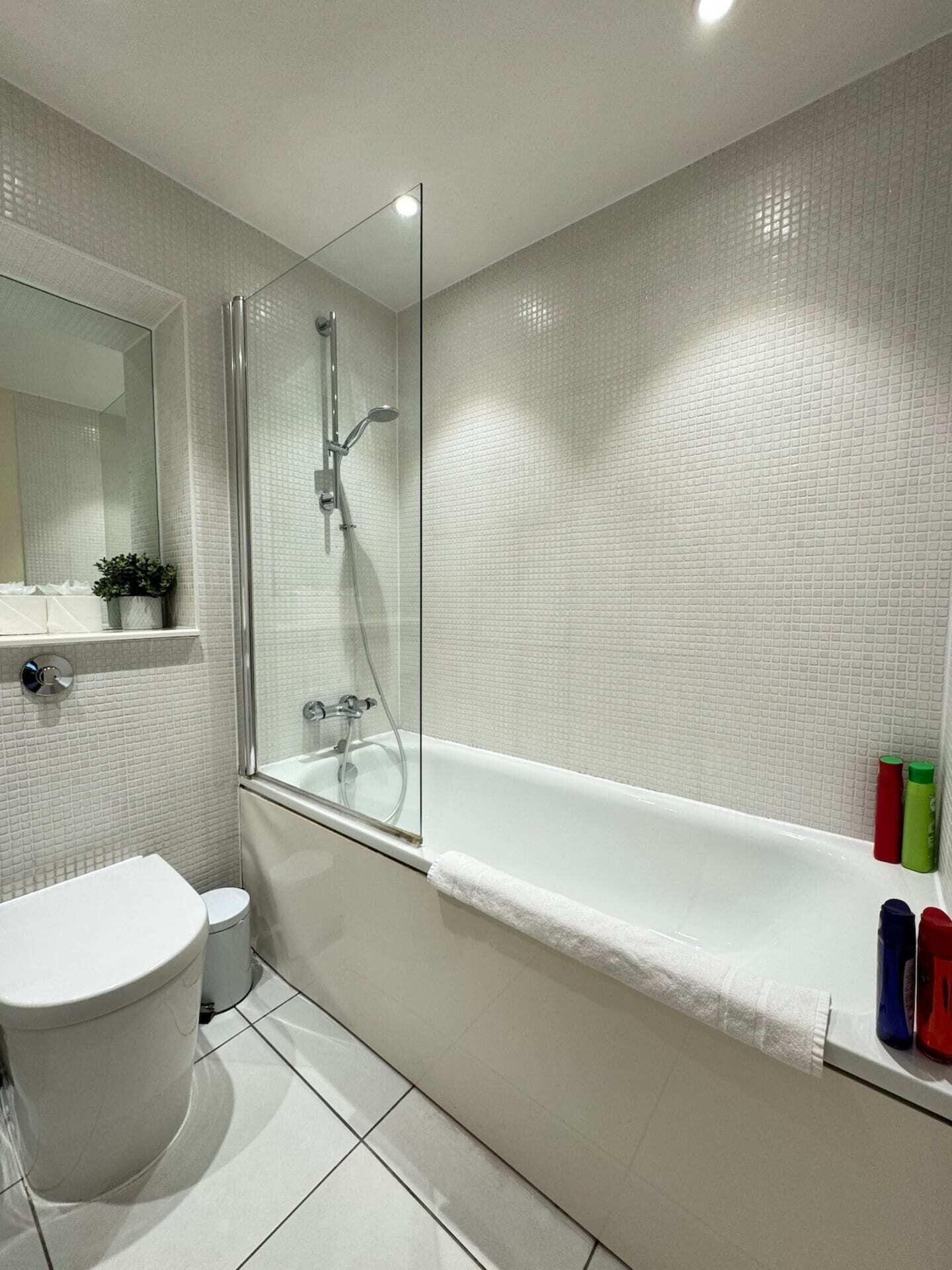 A modern bathroom with a glass-enclosed shower, a white toilet, and a bathtub with a towel.