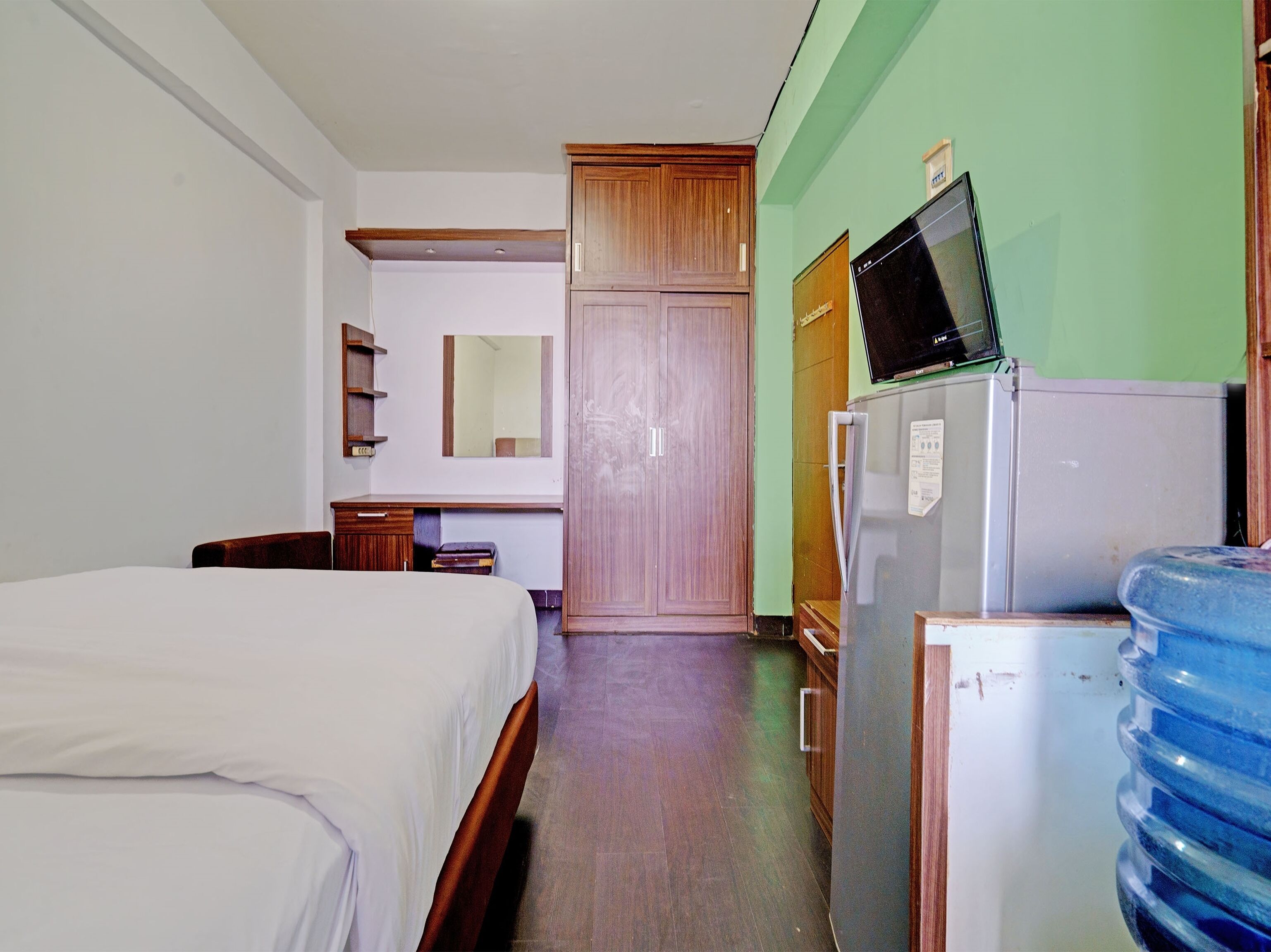A hotel room with a bed, a desk, a wardrobe, a refrigerator, and a water dispenser.