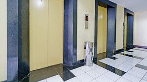 A hallway with yellow doors, a trash can, and a digital elevator display.