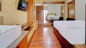 A hotel room with a bed, a desk, a chair, a TV mounted on the wall, and a bathroom with a sink and mirror.