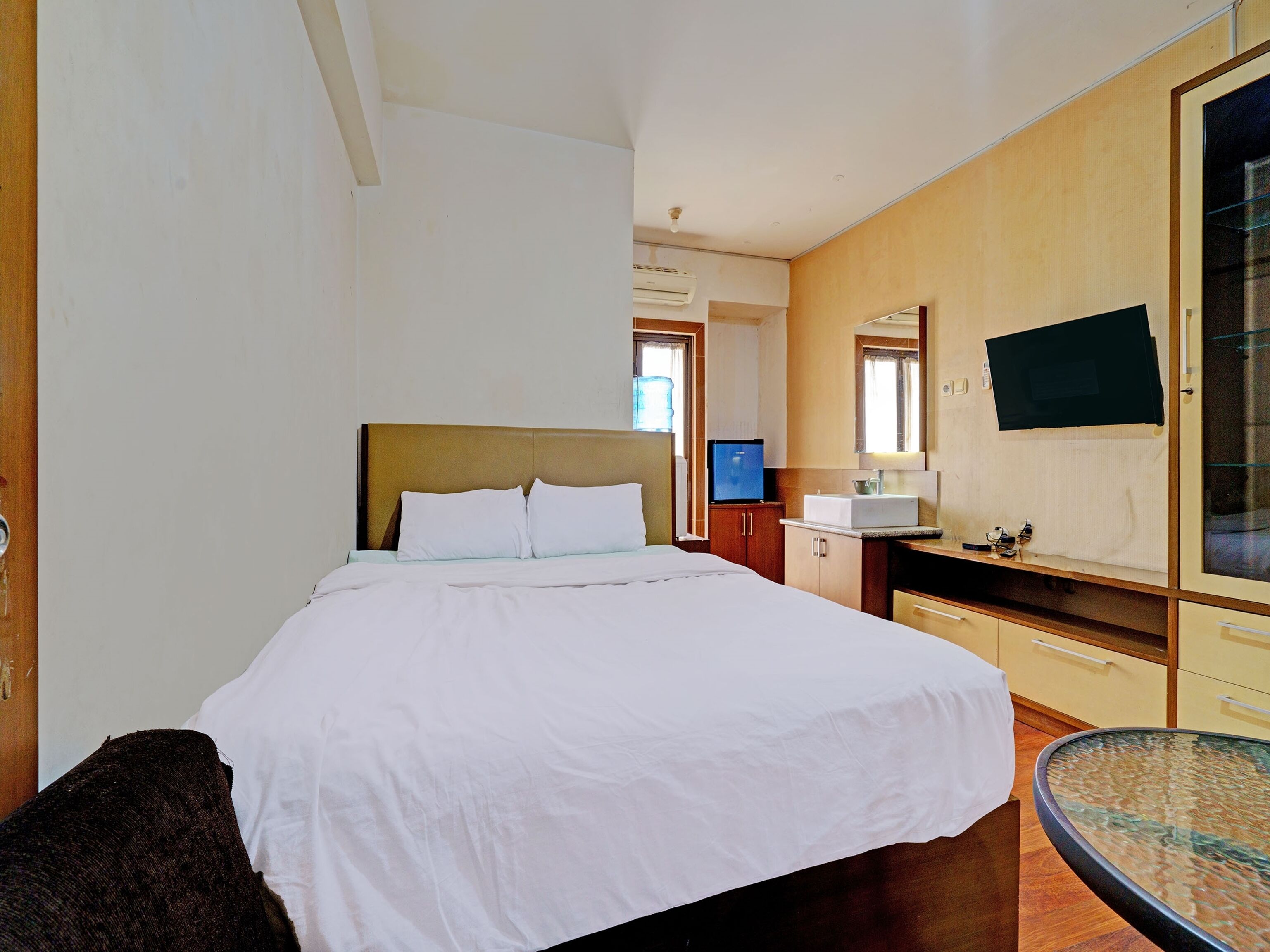 A hotel room with a bed, a small table, a TV, a sink, and a mirror.