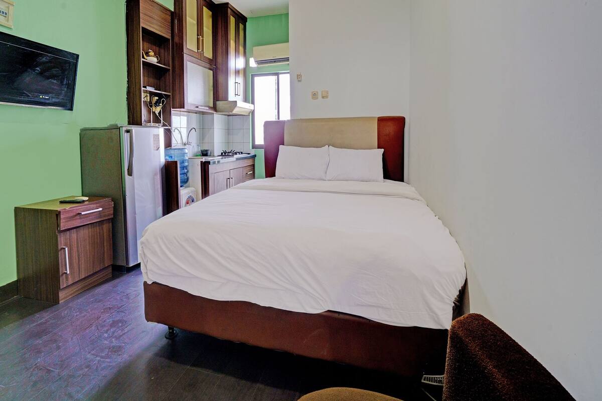 A compact room with a bed, a small kitchenette, and a TV on the wall.