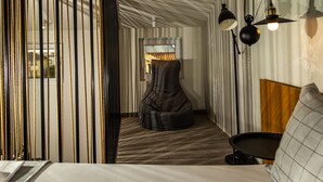 Una habitación de hotel con cama, un sillón informal, una mesita y un espejo.