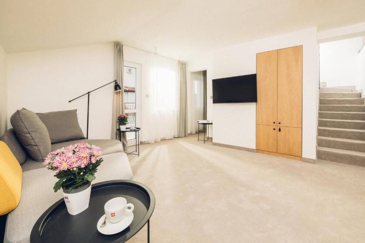 A modern living room with a sofa, a coffee table with a flower vase, a TV mounted on the wall, and a staircase leading to another level.