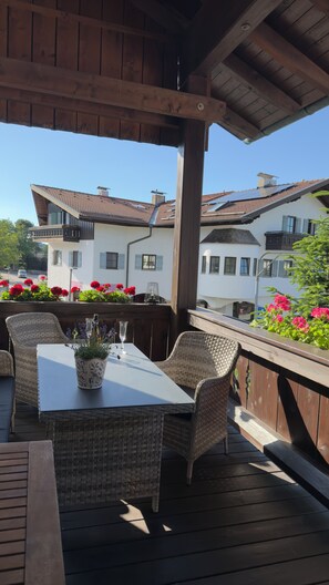 An outdoor patio with wicker furniture, a table with a glass, and potted plants.
