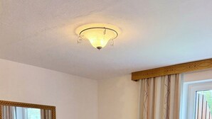 Un dormitorio con un aparador de madera, una silla blanca, una cama con ropa de cama blanca y una lámpara en el techo.