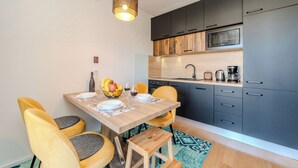 A modern kitchen with dark cabinets, a microwave, and a wooden dining table with yellow chairs. - Apartment Babic (Vir)