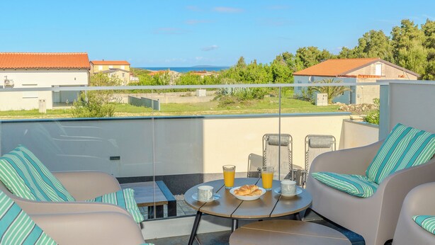 A balcony with two cushioned chairs, a small table, and a breakfast setting including croissants and orange juice. - Apartment Babic (Vir)