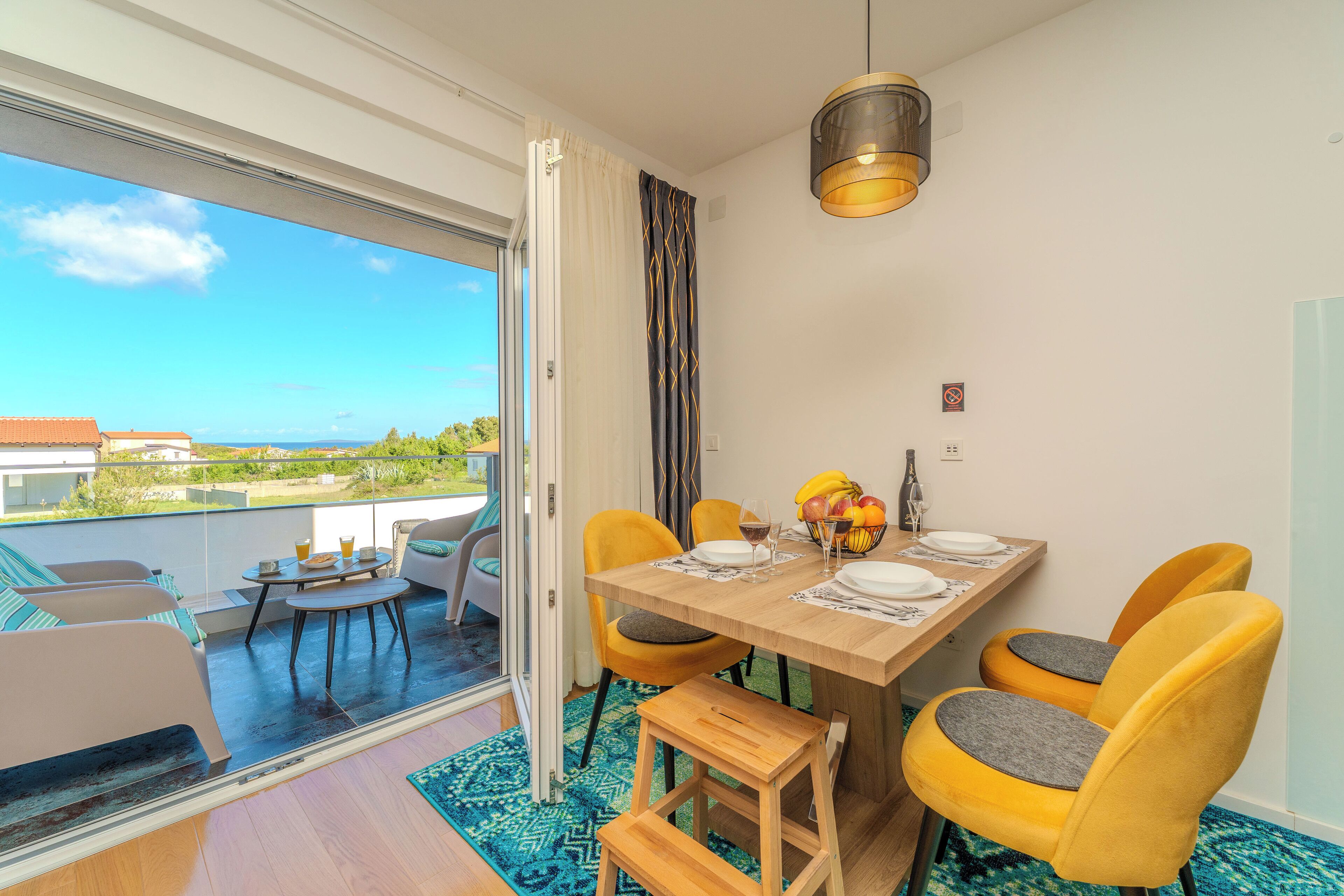 A dining area with a wooden table, yellow chairs, and a view through a glass door to the outdoors.