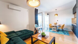 A modern living room with a green sofa, a wooden coffee table, and a dining area with a table and chairs. - Apartment Babic (Vir)