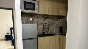 A compact kitchen with a microwave, a refrigerator, wooden cabinets, and a marble backsplash. - Studio Meublés Haut Standing À Bonamoussadi (Douala)