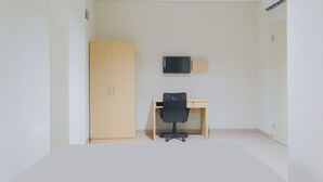 A room with a wooden wardrobe, a desk with a chair, and a mounted television. - OYO Life  92936 Kost Teteh Erni Karawang (Karawang)