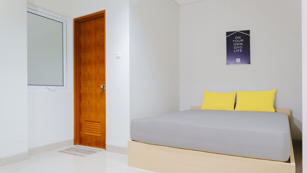 A bedroom with a bed, a wooden door, and a poster on the wall. - OYO Life  92936 Kost Teteh Erni Karawang (Karawang)