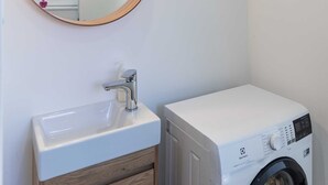 A bathroom with a round mirror, a sink, and a front-loading washing machine. - Room Odin (Dubrovnik)