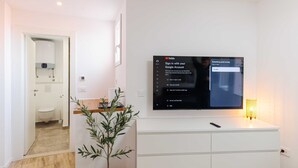A modern living room with a flat-screen TV mounted on a white wall, a potted plant, and a small table with a remote control. - Room Odin (Dubrovnik)