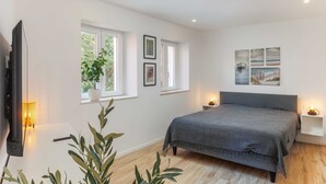 A bedroom with a bed, bedside tables, a TV, windows, and wall art. - Room Odin (Dubrovnik)
