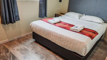 A neatly made bed with a white and red bedspread, two towels, and a small nightstand with a lamp.