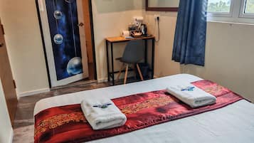 Habitación de hotel con cama, escritorio, silla, televisor y ventana con cortinas.