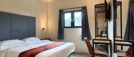 A modern hotel room with a large bed, a desk with a chair, a TV, and a window with curtains.