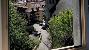 A window view of a town with a church tower and snow-capped mountains in the background.