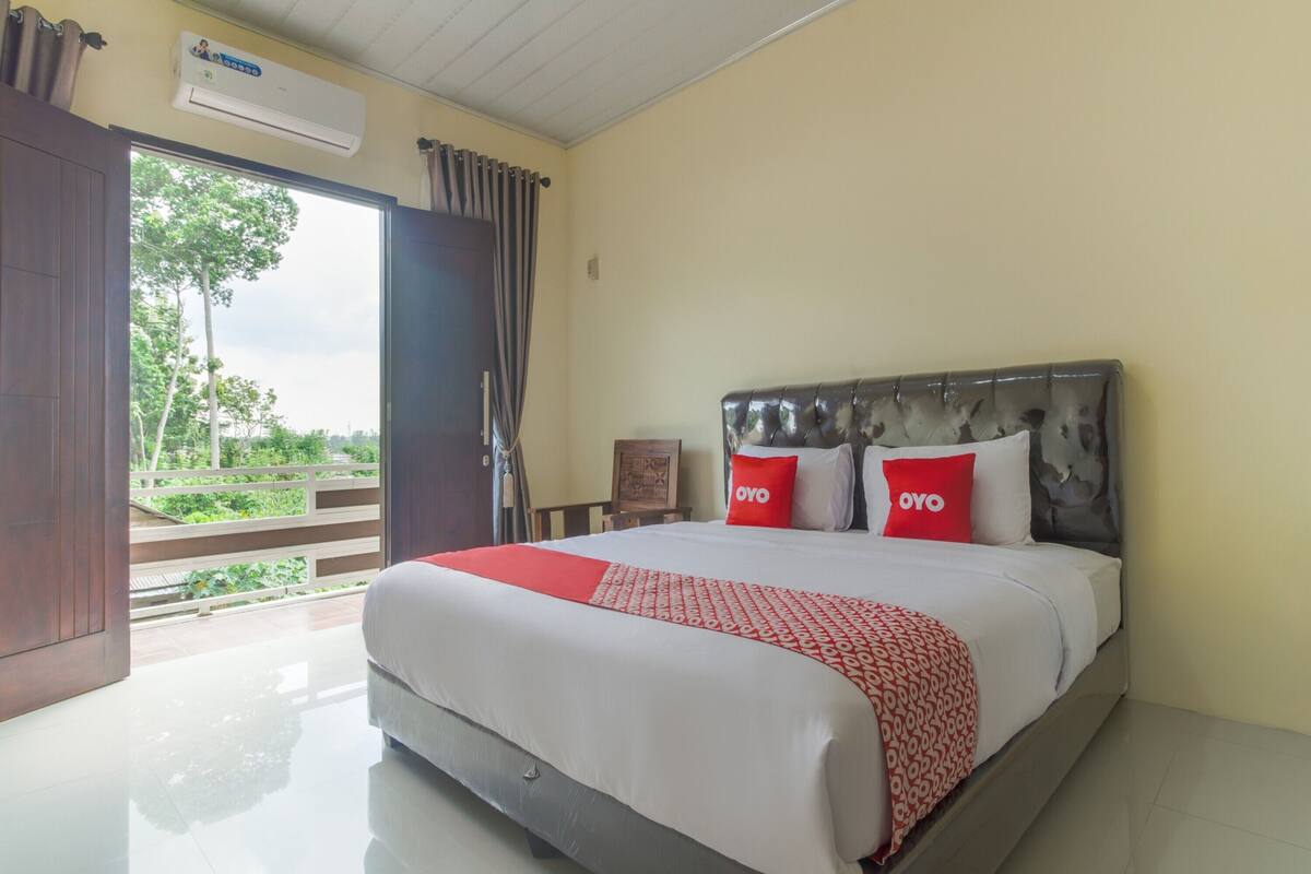 Habitación de hotel con cama, ventana con cortinas, equipo de aire acondicionado y vista a zonas verdes.