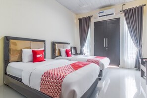 A hotel room with two beds, each with a headboard, white bedding, and red and white patterned blankets. There is a desk with a chair, a wardrobe, and a window with curtains. - OYO Life 3365 Griya Nusantara Syariah (Bandar Lampung)