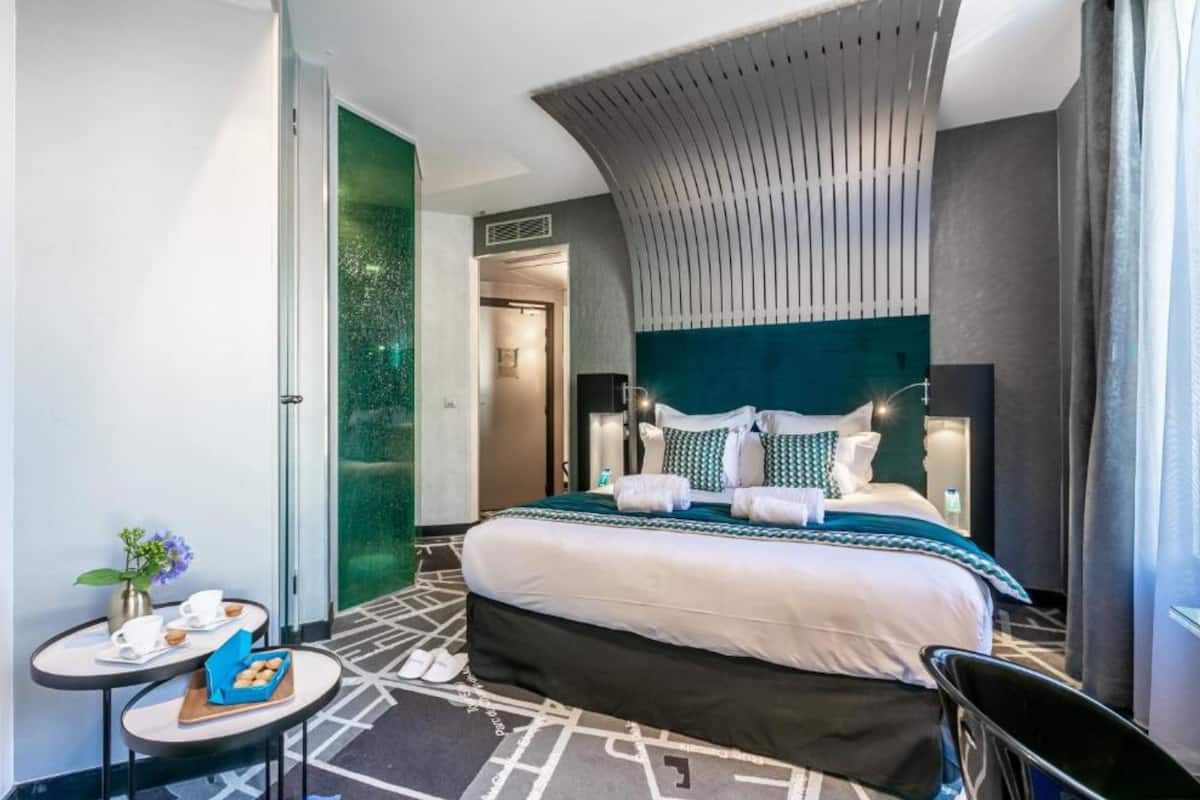 A modern hotel room with a large bed, a small table with breakfast items, and a unique ceiling design.