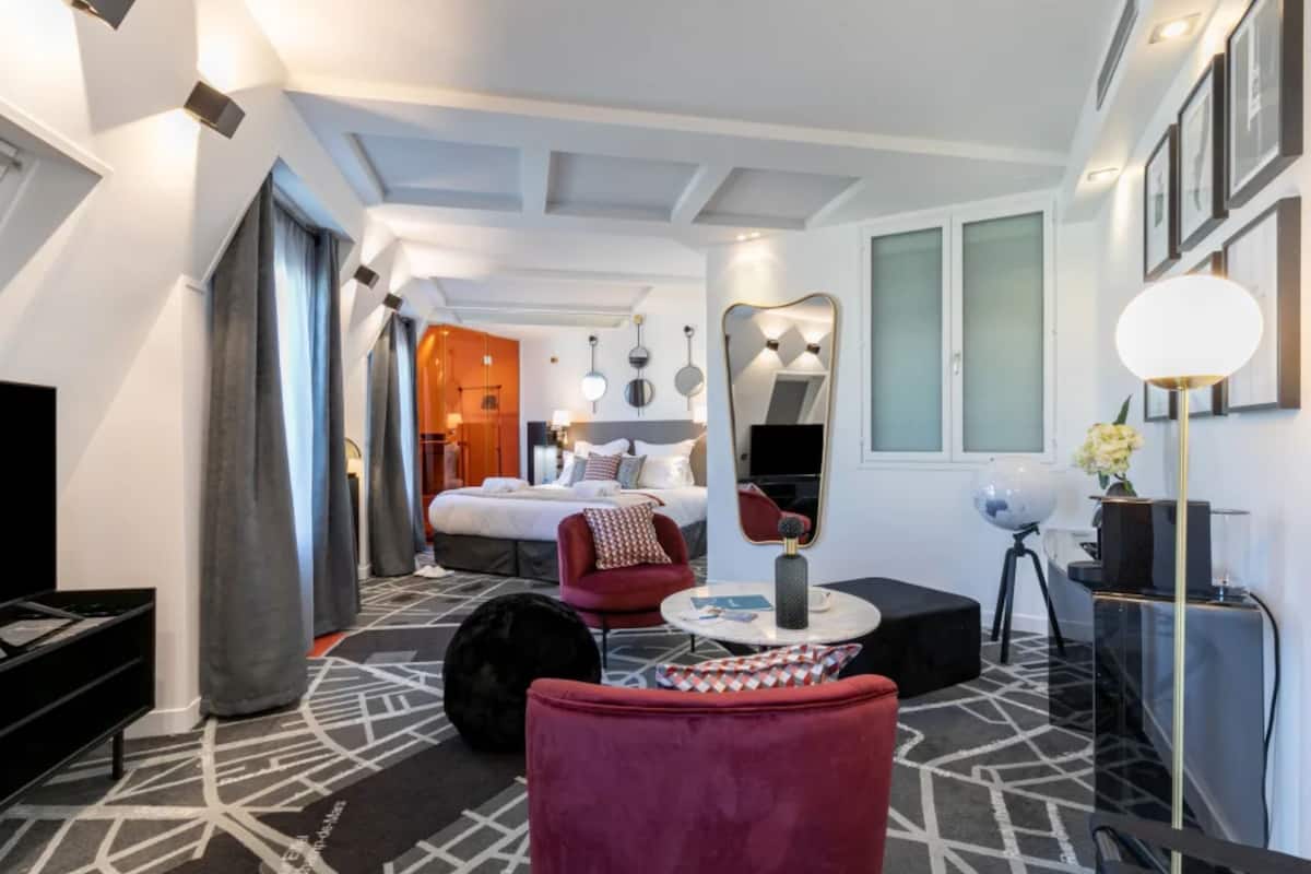 A modern hotel room with a large bed, a red armchair, a round coffee table, and a globe on a tripod.