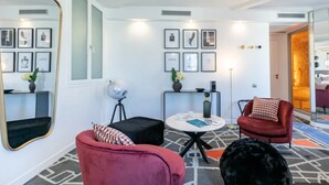 A modern hotel room with a large mirror, framed artwork, a round table, and a red armchair. - Sublim by Sweet Inn Paris (Paris)