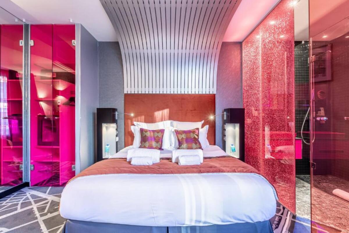 A modern hotel room with a large bed, a curved ceiling, and a glass shower area.
