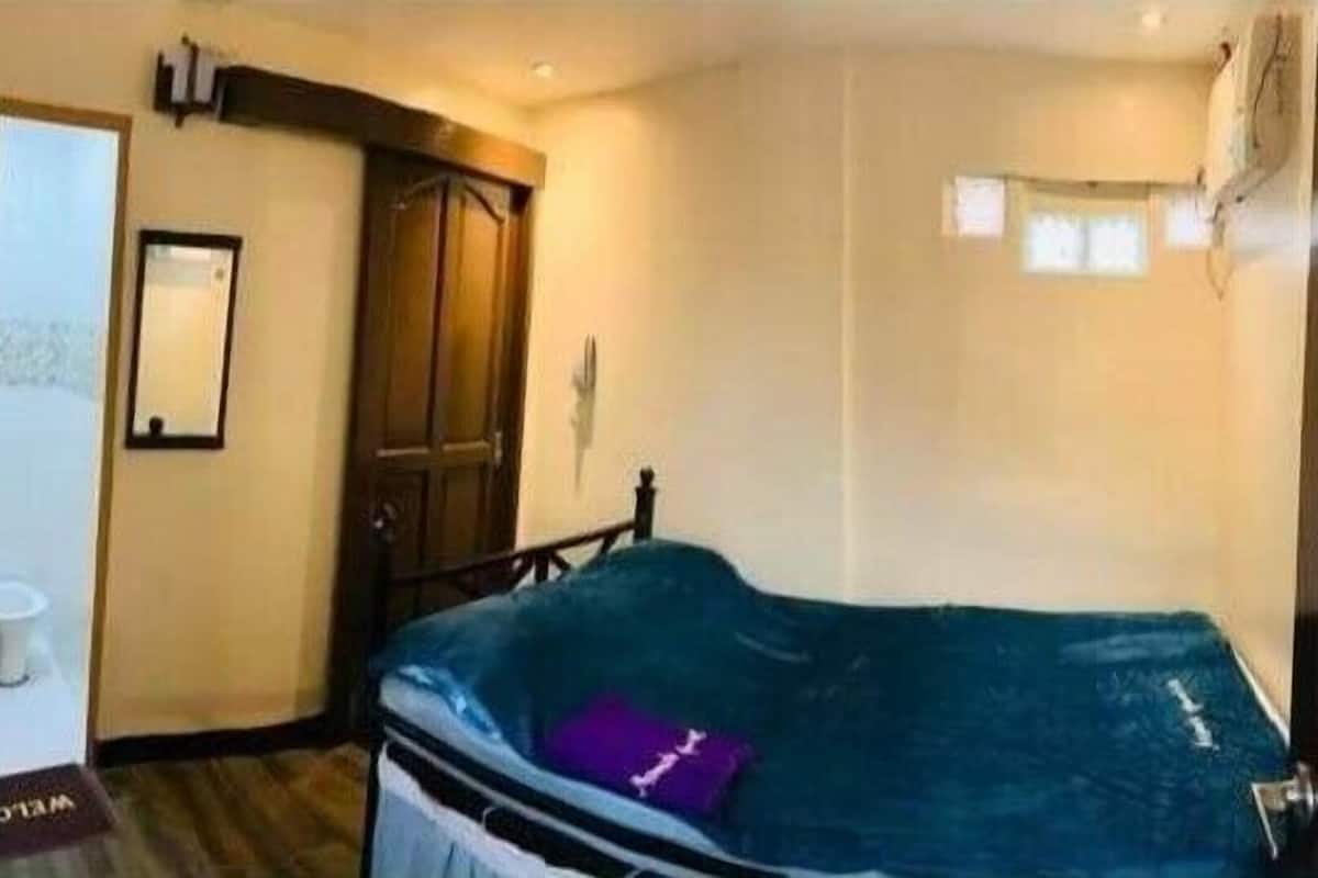 A room with a bed, a door, and a small table with a cup.