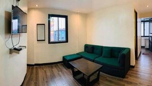 Un saló amb un sofà verd, una taula de centre, televisió penjada a la paret i una finestra.