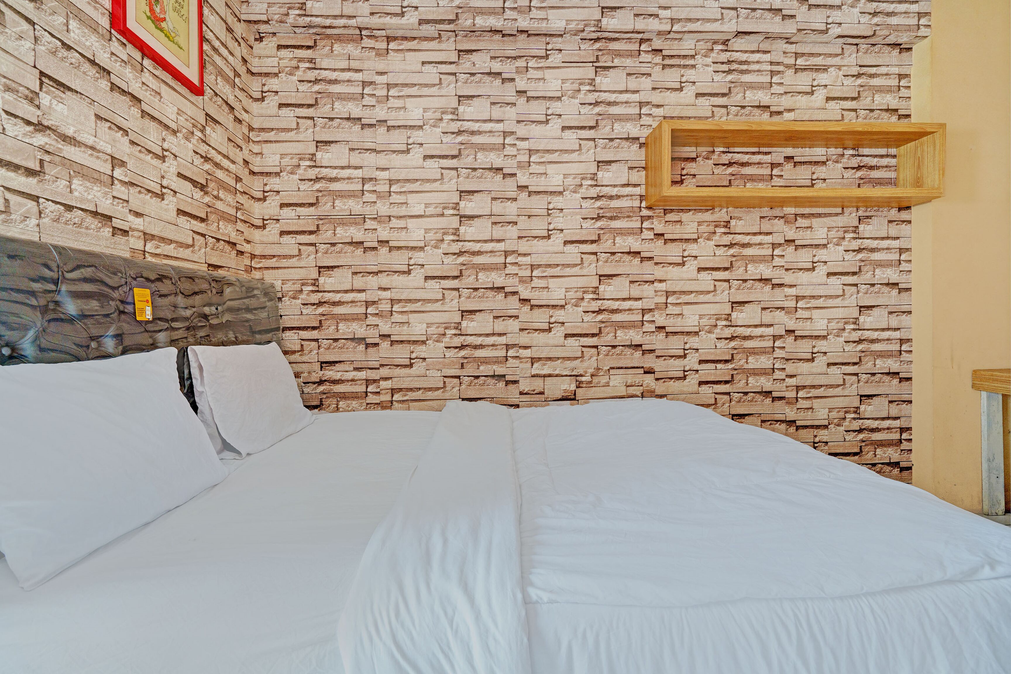 A neatly made bed with white linens, a stone-patterned wall, and a wooden shelf.